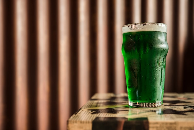 Glass of green drink on table near wooden wall