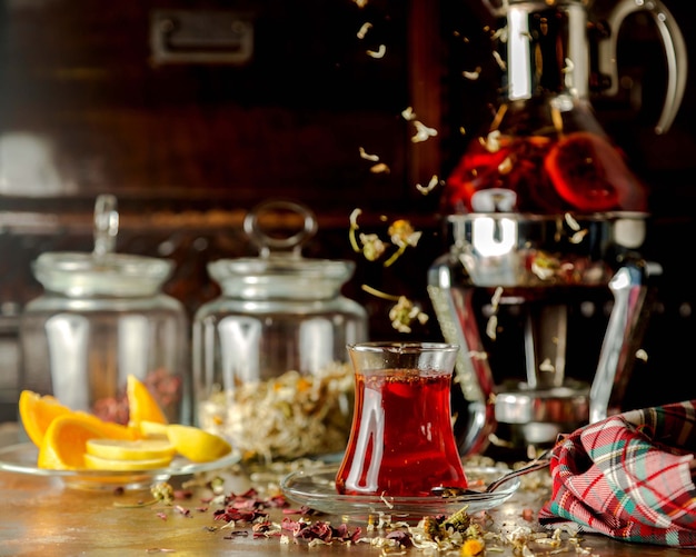 glass of herbs tea next to lemon slices and glass tea pot