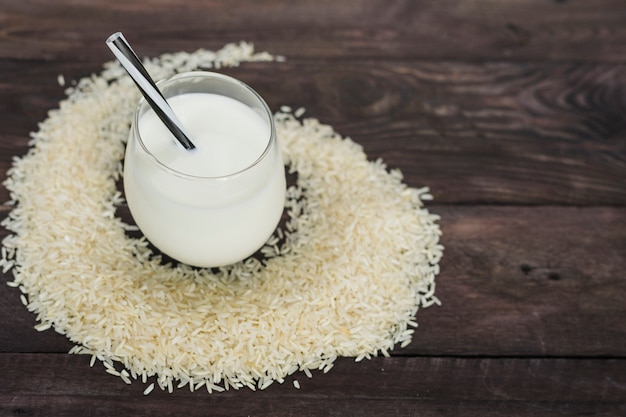 Glass of homemade rice milk decorated with white raw rice over wooden table