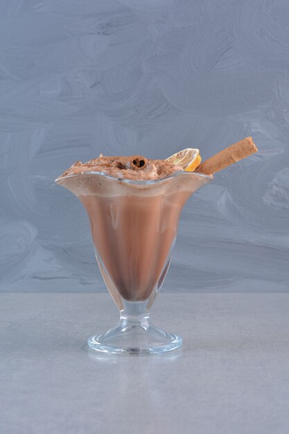 A glass of hot chocolate decorated with cinnamon sticks on stone background.