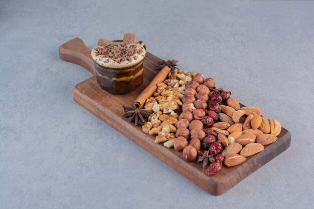 Стакан горячего шоколада с кучей различных орехов на деревянной доске.