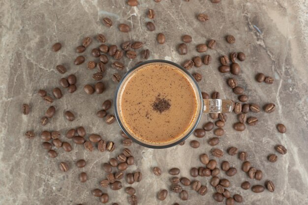 Glass of hot coffee and coffee beans on marble surface