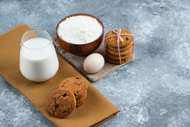 Стакан горячего молока с вкусным печеньем на сером столе.