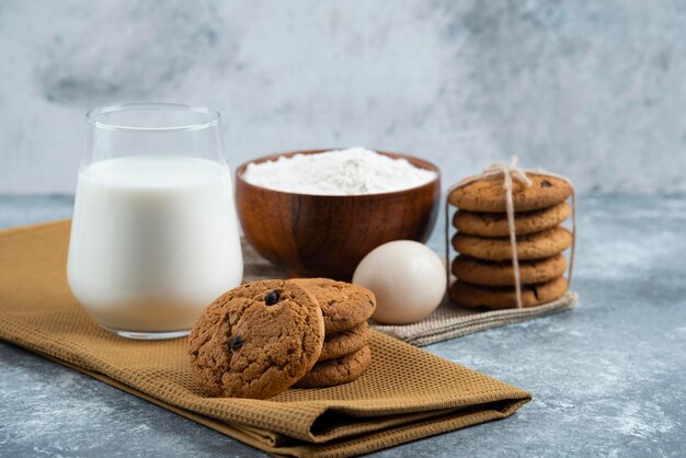 A glass of hot milk with delicious cookies on a gray table.