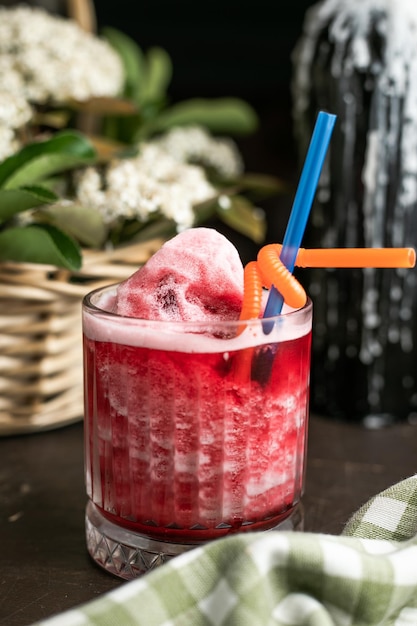 Стакан ледяного коктейля с пипеткой на фоне цветов