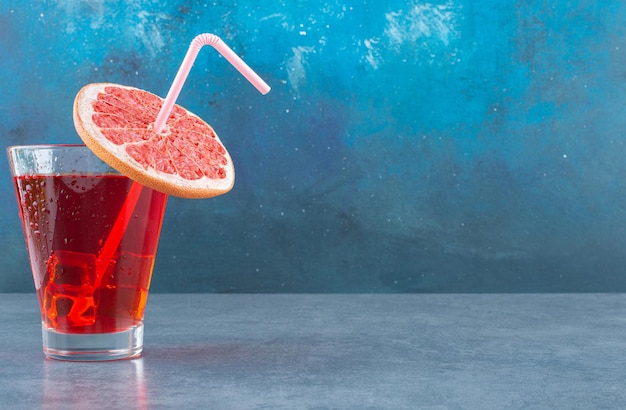 Glass of icy juice with a straw pipe and a slice of grapefruit on blue
