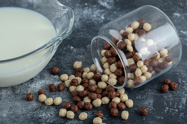 Glass jar of cereal balls and fresh milk on marble.