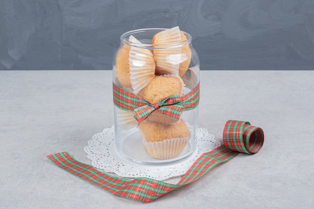 A glass jar of cupcakes on white surface.