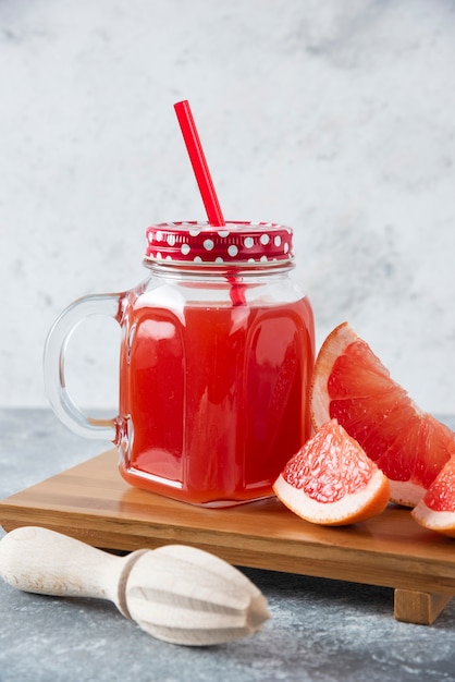 Glass jar of fresh grapefruit juice with slices of fruits and wooden reamer . 