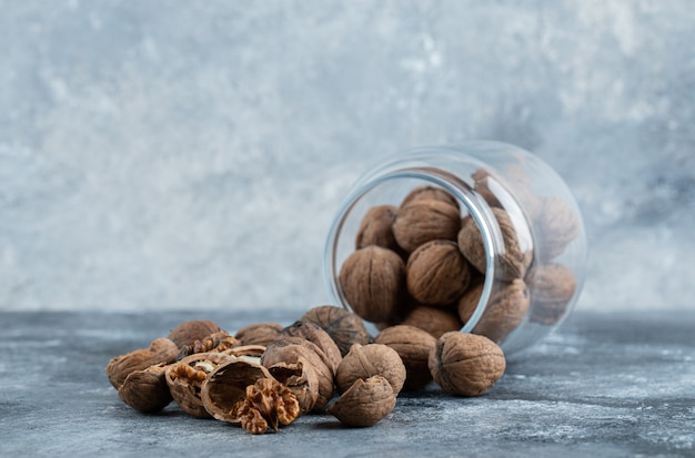 A glass jar full of healthy walnuts on a gray background. 