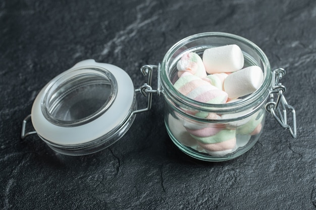 A glass jar full of marshmallows on a dark surface.