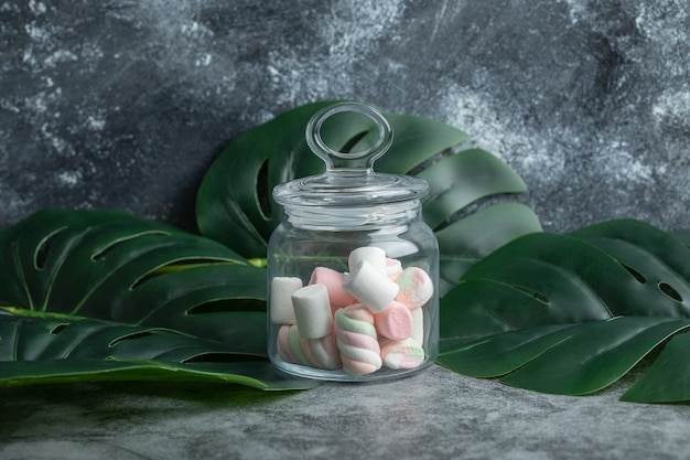 A glass jar full of marshmallows on leaves.