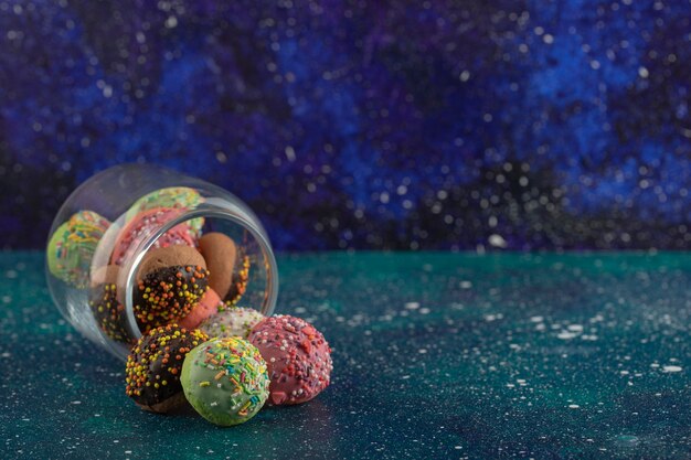Стеклянная банка, полная маленьких разноцветных пончиков.