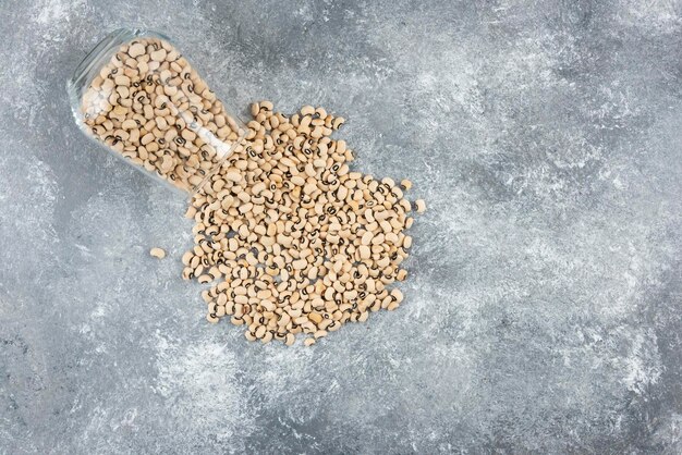 A glass jar full of white raw kidney beans on a gray table.