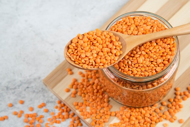 Free photo glass jar of red lentils with wooden spoon on wooden board.