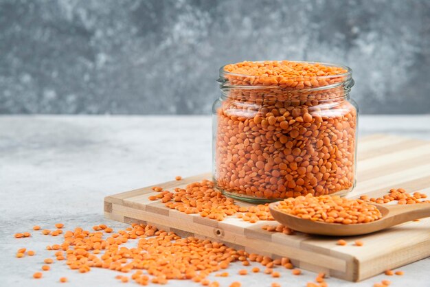 Glass jar of red lentils on wooden board.