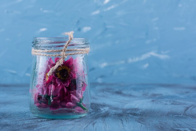 A glass jar with artificial purple flowers on blue.