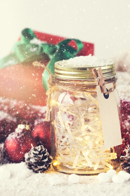 Vaso di vetro con luci e le decorazioni di natale con neve intorno