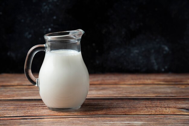 Glass jug of fresh milk on wooden table. 