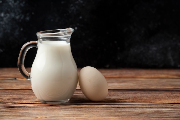 Glass jug of milk and egg on wooden table. 