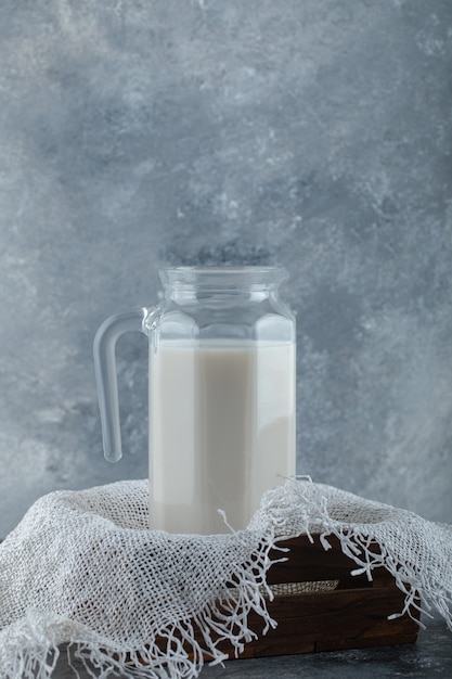 Glass jug of milk in wooden box with burlap.
