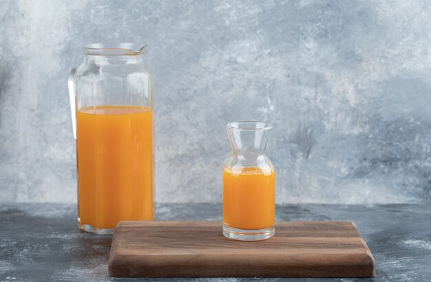 Glass and jug of orange juice on wooden board. 