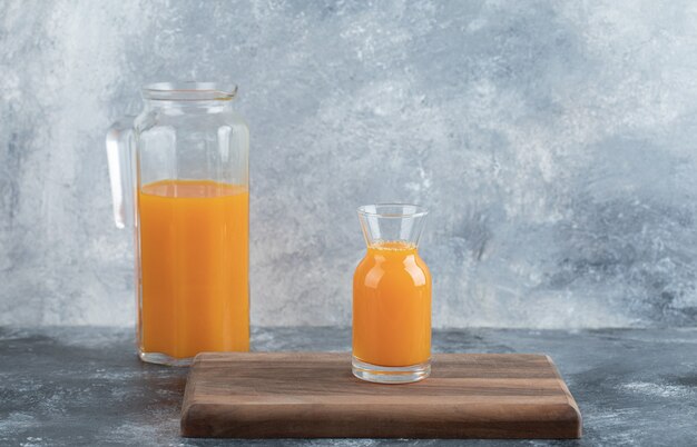 Glass and jug of orange juice on wooden board. 