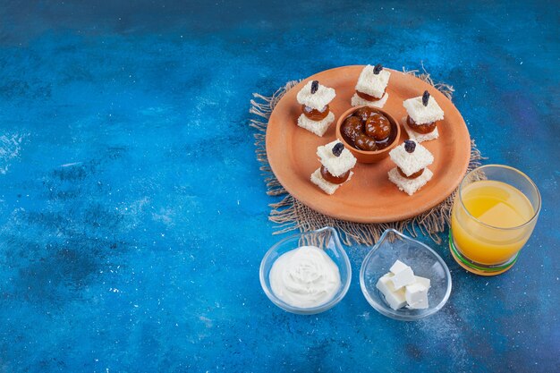 A glass of juice and fig jam on a plate next to bowls of cheese, on the blue table.