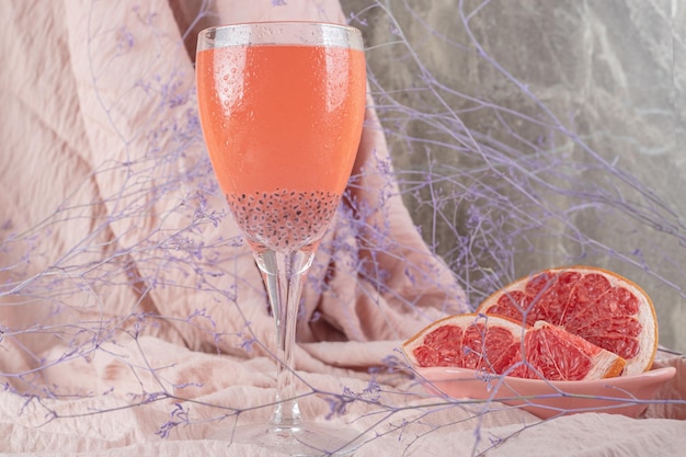 A glass of juice and fresh grapefruit on pink cloth. 