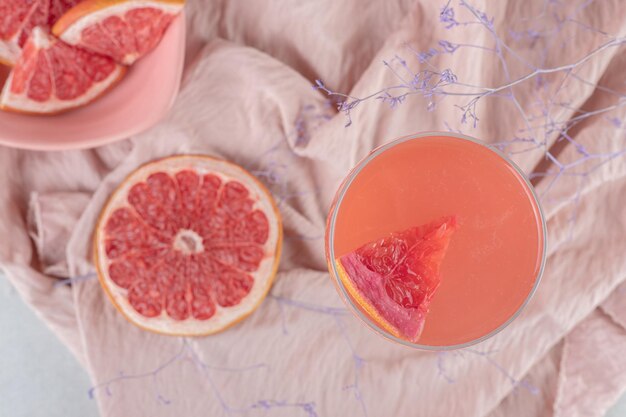 Стакан сока и свежий грейпфрут на розовой ткани