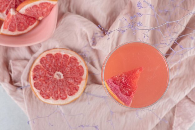 A glass of juice and fresh grapefruit on pink cloth