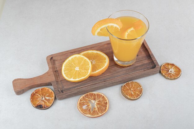 A glass of juice and orange slices on wooden board