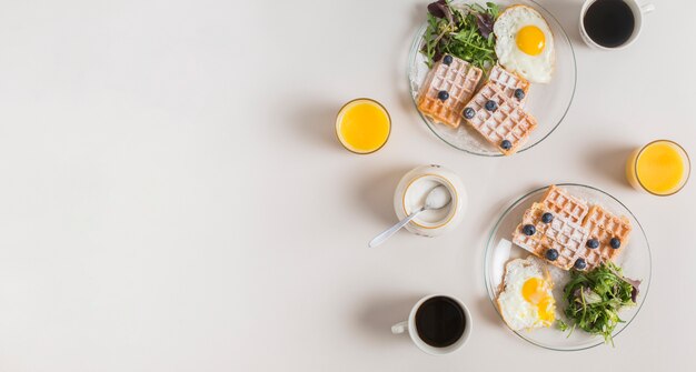 Glass of juice; powdered milk; tea and healthy salad with waffle and fried eggs on plate over white backdrop