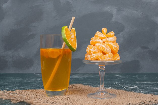 Glass of juice and slices of tangerine on marble wall .