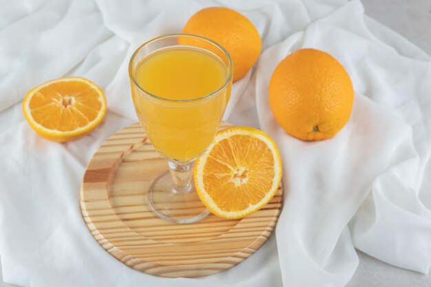 A glass of juice with fresh oranges on wooden plate