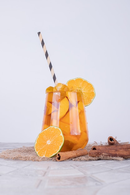 A glass of juice with fruit slices and cinnamon on white wall.