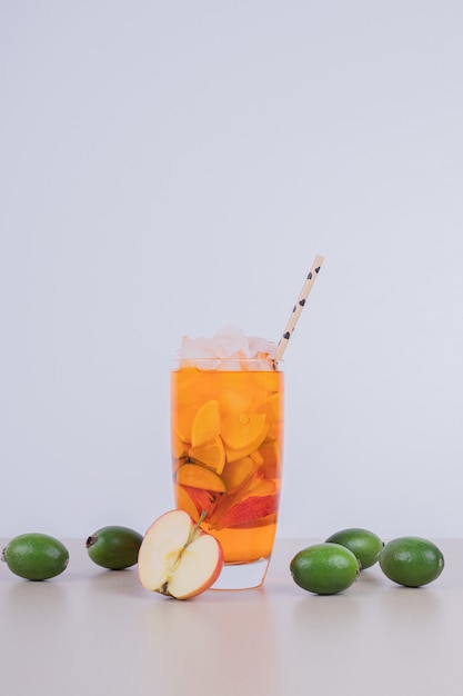 A glass of juice with fruit slices and fresh fruits.