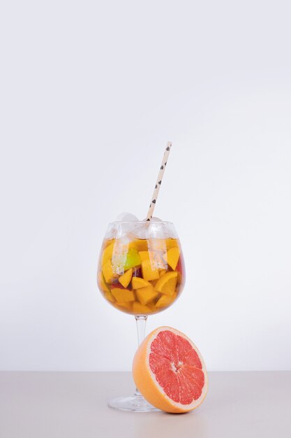 A glass of juice with fruit slices and grapefruit on white wall.