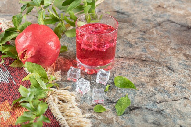 Glass of juice with ice cubes and pomegranate on stone surface