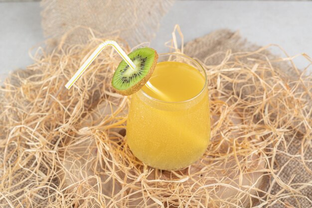 A glass of juice with kiwi slice and straw on burlap. 