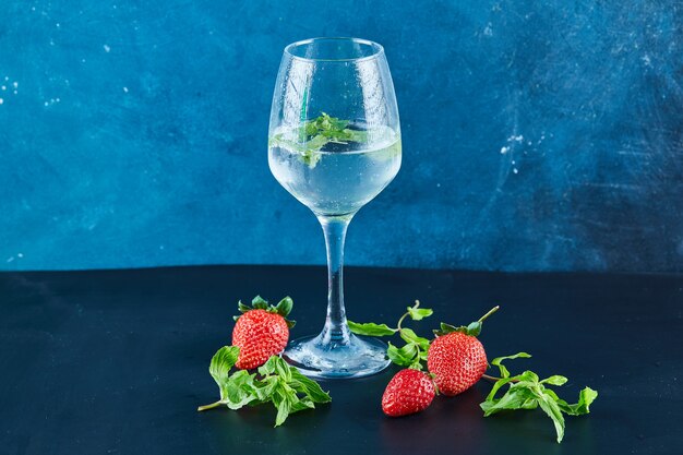 A glass of juice with mint and fresh strawberries and mint on blue surface