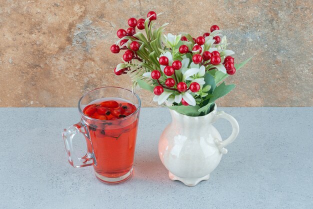 Glass of juice with rosehips and artificial flowers on blue table. High quality photo