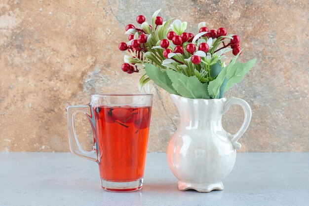 Glass of juice with rosehips and artificial flowers on blue table.