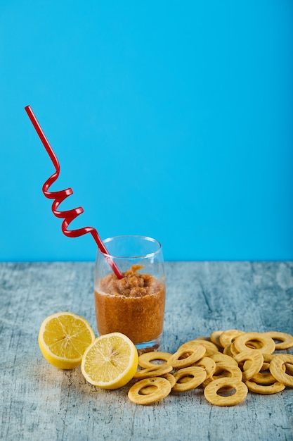 A glass of juice with straw, lemons and crackers on gray table. 