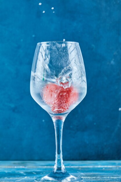 A glass of juice with strawberry inside on blue surface