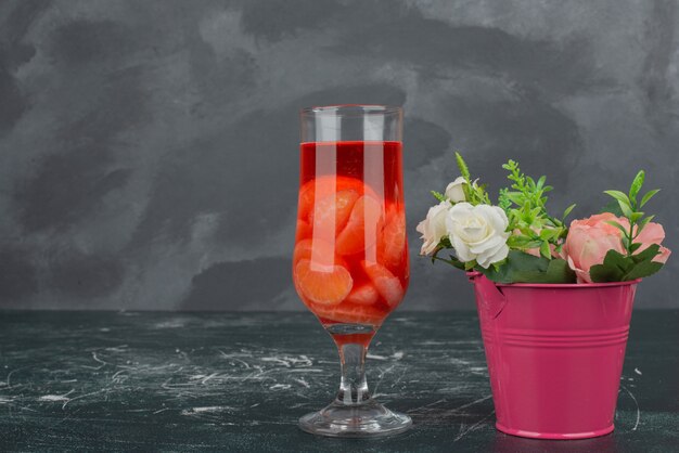 Glass of juice with tiny bucket on marble table.