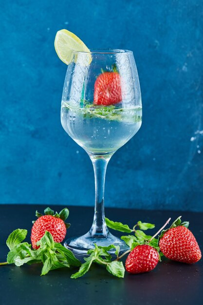 A glass of juice with whole fruits and slice of lemon inside on dark surface