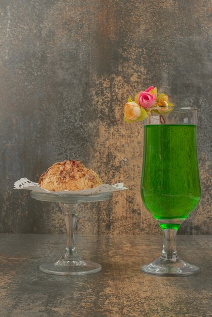 A glass of juicy green lemonade and piece of cake on white plate