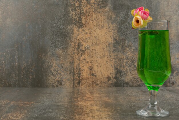 A glass of juicy green lemonade and roses on marble surface. 