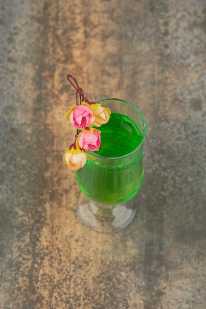 A glass of juicy green lemonade and roses on marble wall.